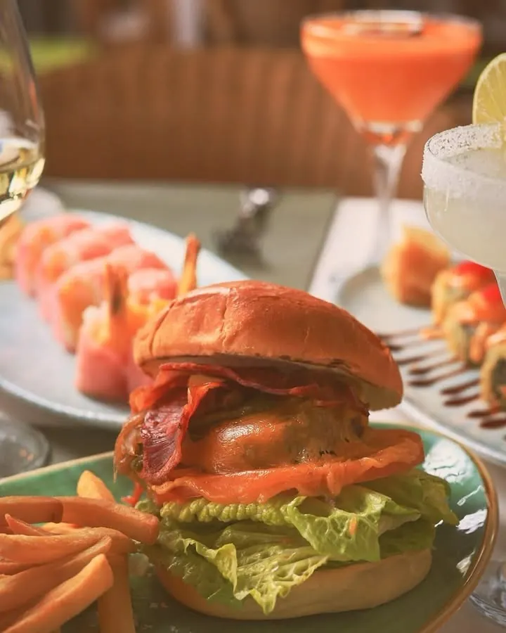 A burger with fries next to sushi and a cocktail