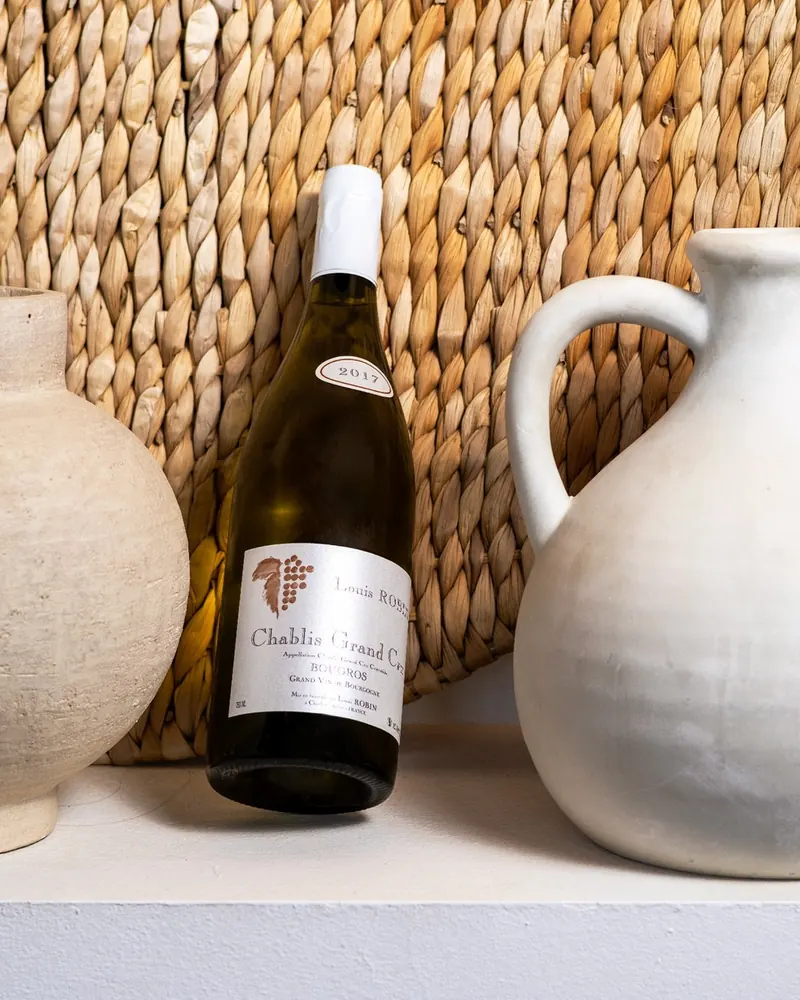 A bottle of Chablis beside clay jugs against woven rattan