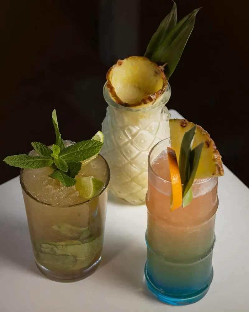 Three tropical cocktails garnished with mint, pineapple and orange