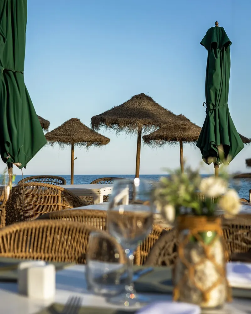 A table at Las Cuchis under palm-leaf umbrellas, looking out to sea