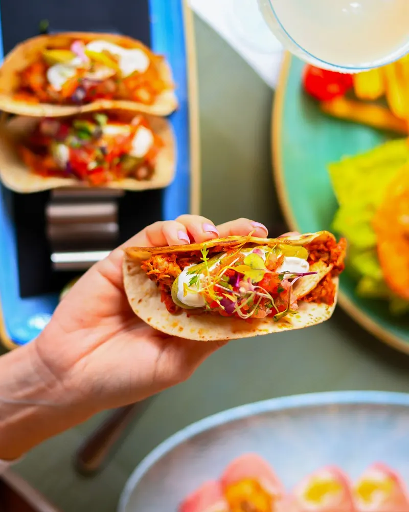Chicken tacos with guacamole and pico de gallo, held over the table