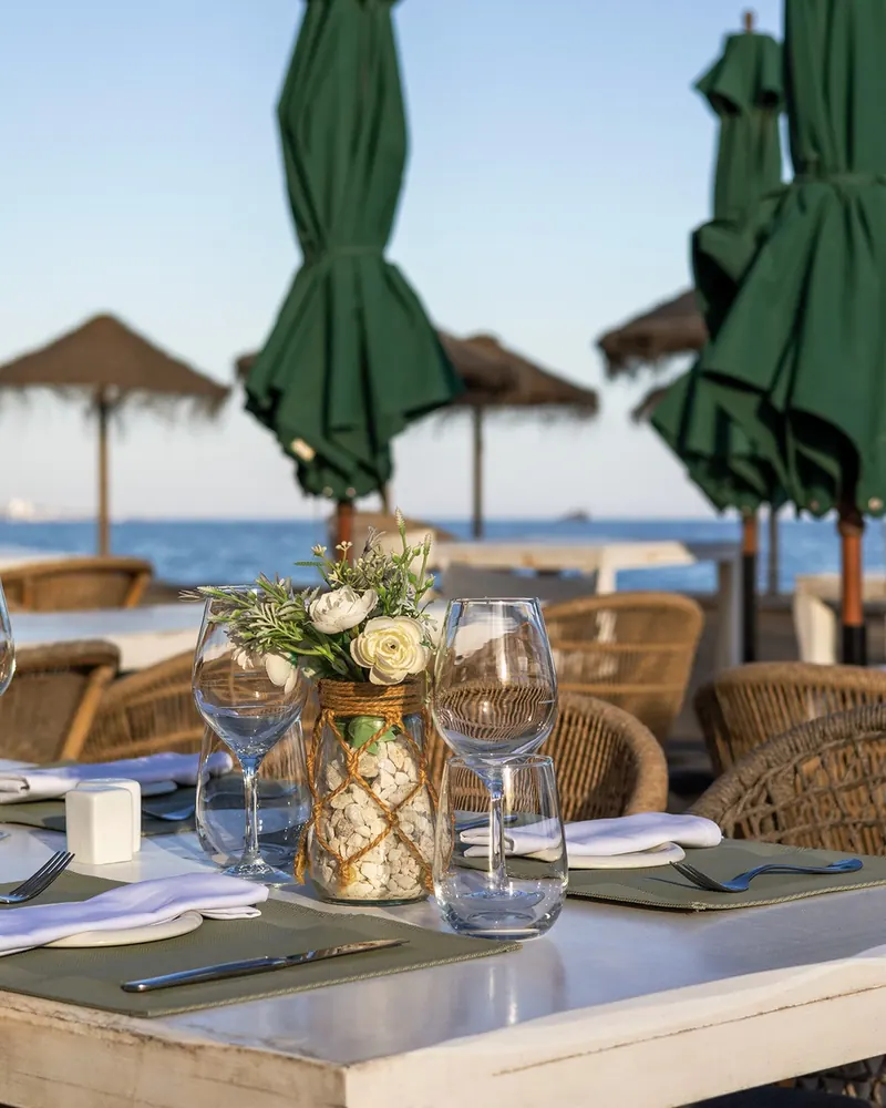 A table laid with flowers and glassware on the terrace, the beach behind
