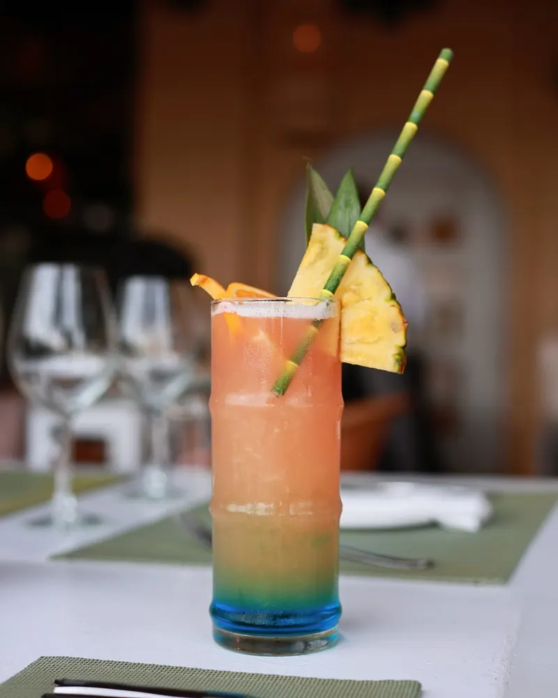A layered tropical cocktail with pineapple and orange garnish